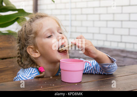 Quattro anni di ragazza cialde per mangiare e bere il tè al tavolo sulla veranda Foto Stock