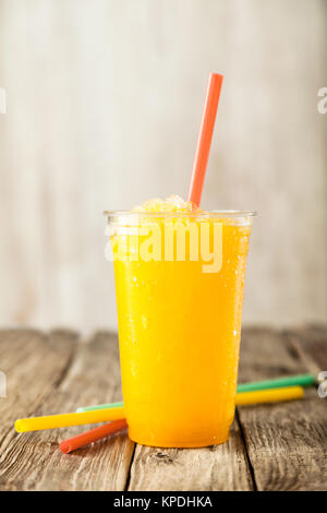 Close Up e rinfrescante Cool arancio brillante Slush drink in una tazza di plastica servita su tavola in legno rustico con una collezione di coloratissimi bere cannucce Foto Stock