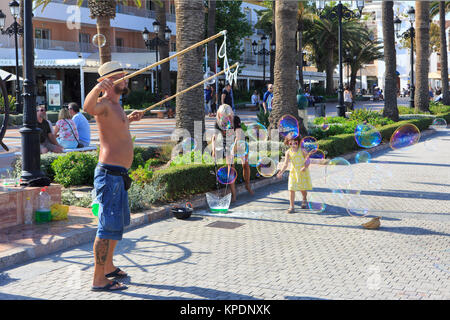 Una piccola ragazza cerca di catturare un enorme bolla di sapone fatto da un esecutore artistico al Balcón de Europa a Nerja sulla Costa del Sol in Spagna Foto Stock