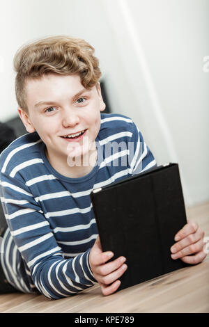 Sorridente ragazzo disteso sul pavimento con computer tablet Foto Stock