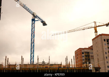 Sagome di gru a torre contro il cielo di sera. Casa in costruzione. Skyline industriale con case in costruzione e gru a torre ancora Foto Stock