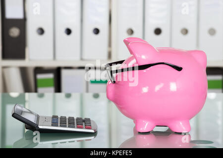 Piggybank indossando occhiali e Calcolatrice sulla scrivania Foto Stock