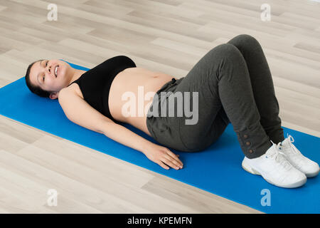 Donna incinta giacente sul tappeto di esercizio Foto Stock