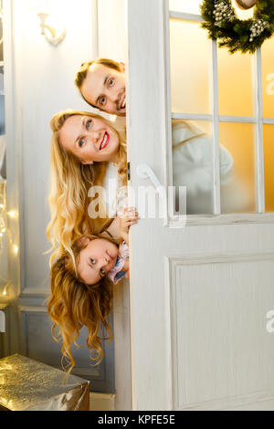 Foto di famiglia felice con la figlia che spuntavano da dietro la porta con la ghirlanda di Natale Foto Stock