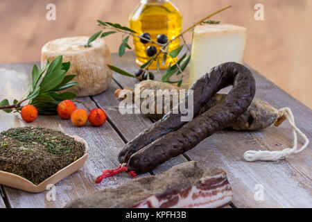 Diverse varietà di Corsica tradizionale di salumi con un ramo di olivo e olive nere su sfondo di legno Foto Stock