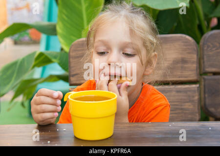 Quattro anni di ragazza divertente panino farcito nella sua bocca e guarda a un bicchiere di tè Foto Stock