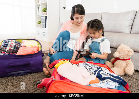 Bellissima ed elegante madre con piccola figlia imballo finito di bagagli e utilizzando mobile digitale compressa cercando informazioni di viaggio. Foto Stock