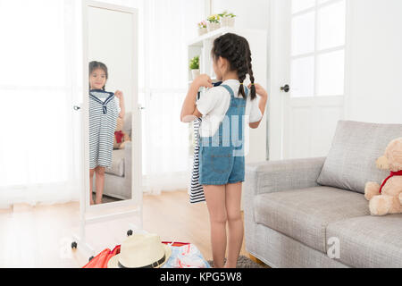 Felice giovane bambina Imballaggio bagagli personali la valigia in casa e guardando lo specchio da viaggio scegliendo i vestiti in salotto. Foto Stock