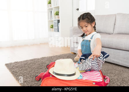 Piuttosto adorabile bambina abiti di piegatura mettere in valigia sul soggiorno piano e imballaggio sacchetto bagagli prepararsi al viaggio durante le vacanze estive. Foto Stock