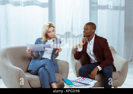 Interracial fotografi scegliendo le foto insieme mentre è seduto in poltrona in ufficio Foto Stock