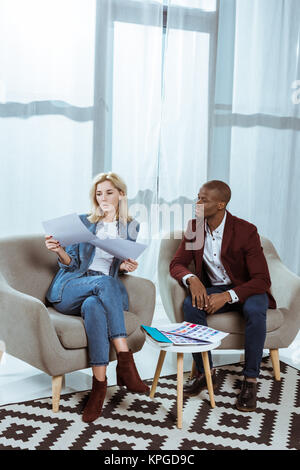 Interracial fotografi scegliendo le foto insieme mentre è seduto in poltrona in ufficio Foto Stock