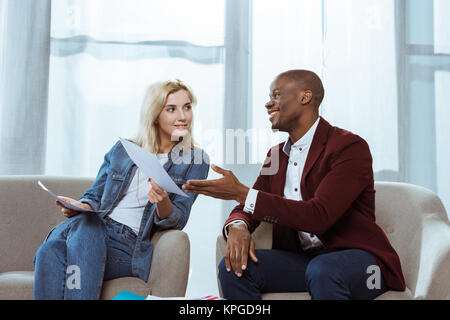 Interracial fotografi scegliendo le foto insieme mentre è seduto in poltrona in ufficio Foto Stock