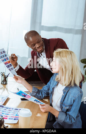 Vista laterale dei fotografi multiculturale scegliendo portfolio insieme al lavoro in ufficio Foto Stock