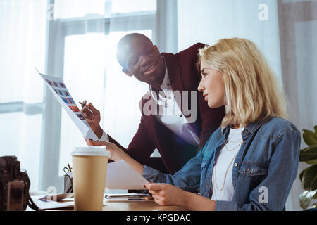 Vista laterale dei fotografi multiculturale scegliendo portfolio insieme al lavoro in ufficio Foto Stock