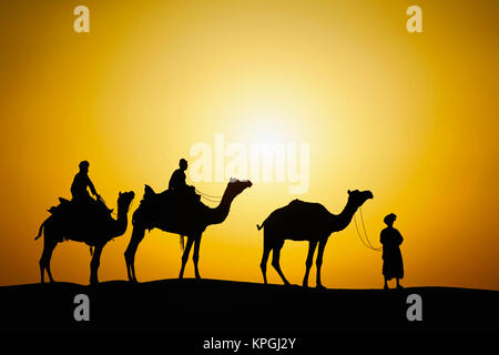 I cammelli e driver di cammello stagliano al tramonto, il Deserto di Thar, Jodhpur, India. Foto Stock