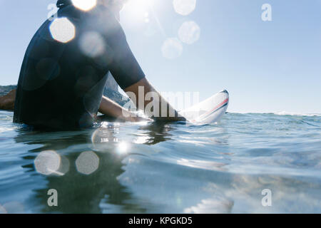 L uomo sulla parte superiore della sua tavola da surf attende un'onda per il surf Foto Stock