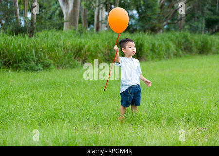 Asian kid di cattura con il suo palloncino arancione Foto Stock