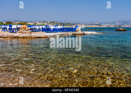 Tavoli con sedie in una tradizionale taverna Greca Kolympia nella cittadina sulla costa dell'isola di Rodi, Grecia. Foto Stock