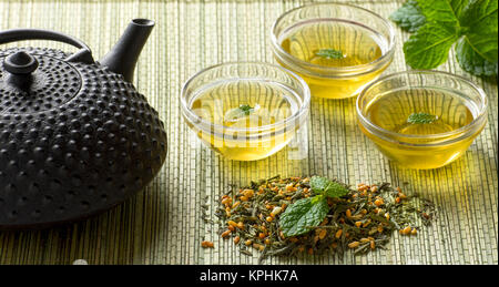Giapponese organico fresco tè verde e foglie di tè con chiara bicchieri e teiera in metallo seduta sul tappetino di bambù sfondo Foto Stock