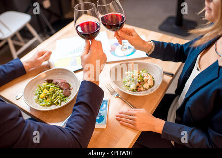 Azienda giovane avente una conversazione durante la cena tintinnanti bicchieri al ristorante Foto Stock