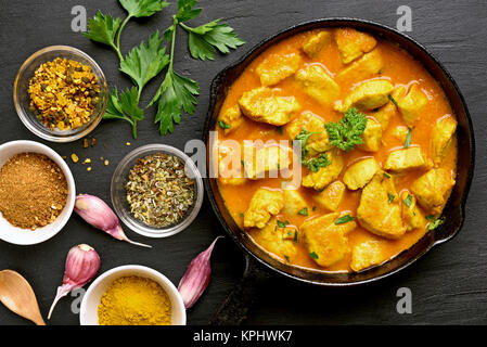 Pollo al curry in padella in pietra scura sullo sfondo. Vista superiore piana e il cibo dei laici Foto Stock