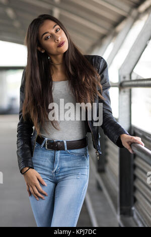Giovane donna con capelli lunghi marrone in jeans e giacca di pelle Foto Stock