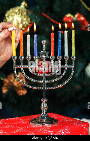 Il Menorah con candele per Hanukkah sullo sfondo del Nuovo Anno Albero. Illuminazione da studio Foto Stock