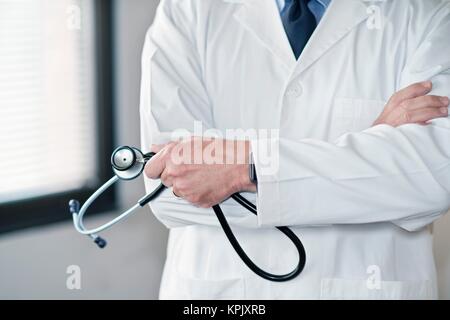 Maschio di dottore in camice bianco con uno stetoscopio, bracci ripiegati. Foto Stock