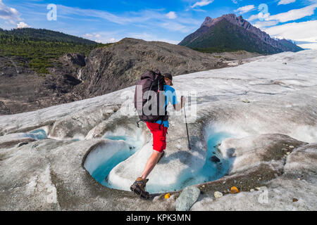 Un backpacker attraversa un flusso sulla superficie del Ghiacciaio di radice in Wrangell-St. Elias National Park. Donoho picco è in background Foto Stock