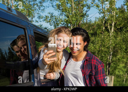 Una giovane coppia prendendo un autoritratto con il loro smart phone al proprio veicolo; Edmonton, Alberta, Canada Foto Stock