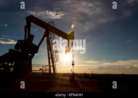 Silhouette di un pumpjack retroilluminati da sole al tramonto sulle praterie Alberta con cielo blu e cloud, a ovest di Airdrie; Alberta, Canada Foto Stock