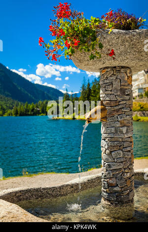 Close-up di una fontana di pietra con vasi di fiori da Champex e la gamma della montagna in background; Champex, Vallese, Svizzera Foto Stock