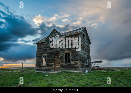 Casa abbandonata su praterie con nuvole temporalesche overhead al tramonto; Val Marie, Saskatchewan, Canada Foto Stock