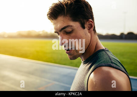 Primo piano di un velocista in piedi su una via di corsa. Runner guardando giù in piedi sulla pista con il sudore che gocciola dalla faccia. Foto Stock