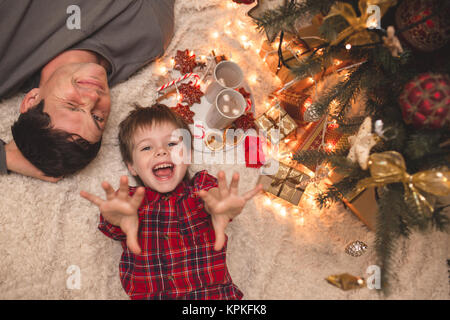 Padre con figlio posa sotto albero di natale con cioccolata e biscotti. Foto Stock