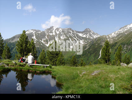 Wanderer un einem kleinen vedere in den Alpen Aurine in Südtirol, Italien; die Berge spiegeln sich in dem kleinen Tümpel; blauer Himmel escursionista presso un piccolo lago nelle Alpi dello Zillertal in Alto Adige, Italia; le montagne sono riflesse nel piccolo stagno; blu cielo Foto Stock