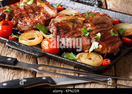 T-bone steak con pomodori e cipolle in una griglia padella close-up su una tavola orizzontale. Foto Stock