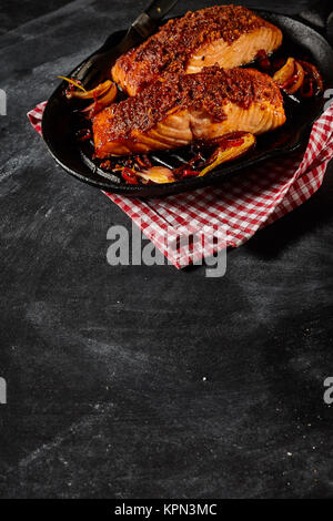 Piccante salmone al forno il piatto per uno in ghisa nera pan su rosso e bianco tovagliolo a scacchi con copia spazio nella zona del tavolo Foto Stock