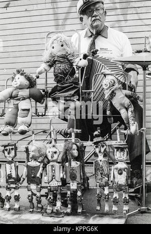 One man band, uomo vecchio con il volto triste e riproduzione di formare fisarmonica e operando una strana impostato con dancing dolls, Dublino, Irlanda. 1989 Foto Stock