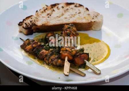 Grigliata di cozze cotte con aglio servita con alcune fette di pane abbrustolito. Foto Stock