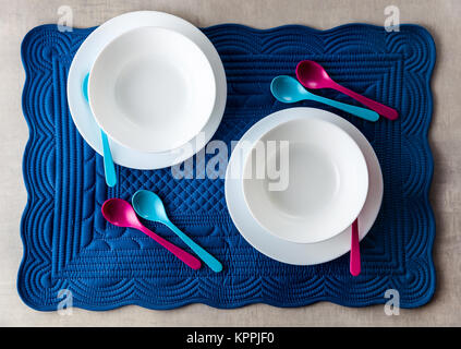 Una serie di piatti per bambini su un morbido blu igienico per colazione. Cucina Accessori tavola per servire. Colorate cucchiai di piccole dimensioni. Foto Stock