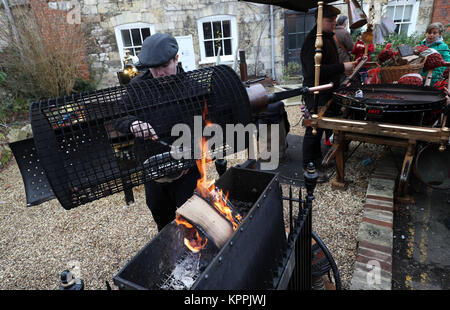 Le castagne vengono arrostite su un fuoco aperto al mercato di Natale nella motivazione della Cattedrale di Winchester in Hampshire, l'ultima settimana prima di Natale. Foto Stock