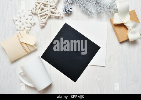 Mockup nero Natale greeting card lettera nella busta e mug, flatlay su un bianco sullo sfondo di legno, con posto per il vostro testo. Piatto, laici top view photo mock up Foto Stock