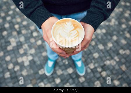 Caffè del mattino sulla strada della citta'. Le mani del giovane azienda tazza monouso con caffè caldo. Foto Stock