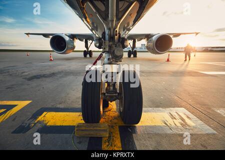 Aeroporto al tramonto da favola. Basso angolo di visione del velivolo all'aeroporto contro. Membro del personale di terra preparando il passeggero aereo befo Foto Stock