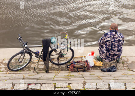 L'uomo pesca dalle rive del fiume Vistola nel medievale città polacca di Torun in Polonia con la sua bicicletta in corrispondenza del lato di lui Foto Stock