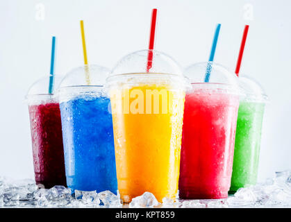 Ancora vita Profilo di frutta congelata granite granita di bevande in plastica tenere lontano le tazze con coperchi e bere cannucce di refrigerazione a freddo sulla superficie metallica con sparsi di cubetti di ghiaccio Foto Stock