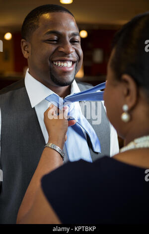 Madre aiutare suo figlio legare il suo tirante. Foto Stock