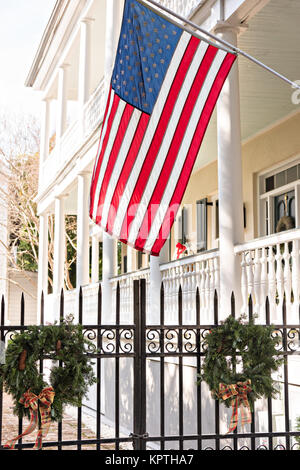 Una bandiera americana è appeso sopra il Natale ghirlande sulla cancellata in ferro battuto di una casa storica su Church Street a Charleston, Sc. Foto Stock