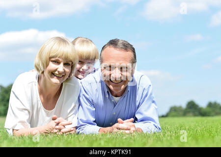 La famiglia felice di tre sdraiati sull'erba. Foto Stock